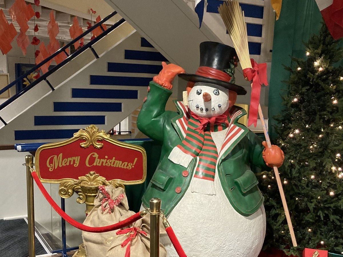 Grote sneeuwman met 'Merry Christmas'-bord, kerstboom en cadeaus