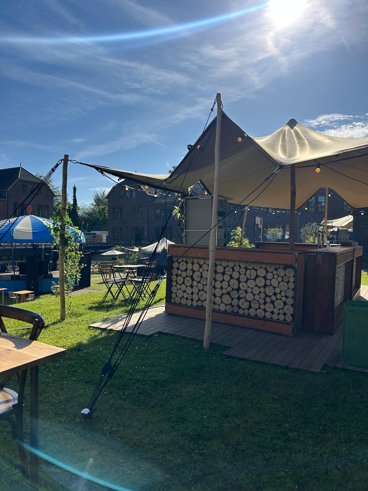Bar op een houten dek met sfeerverlichting onder een stretchtent
