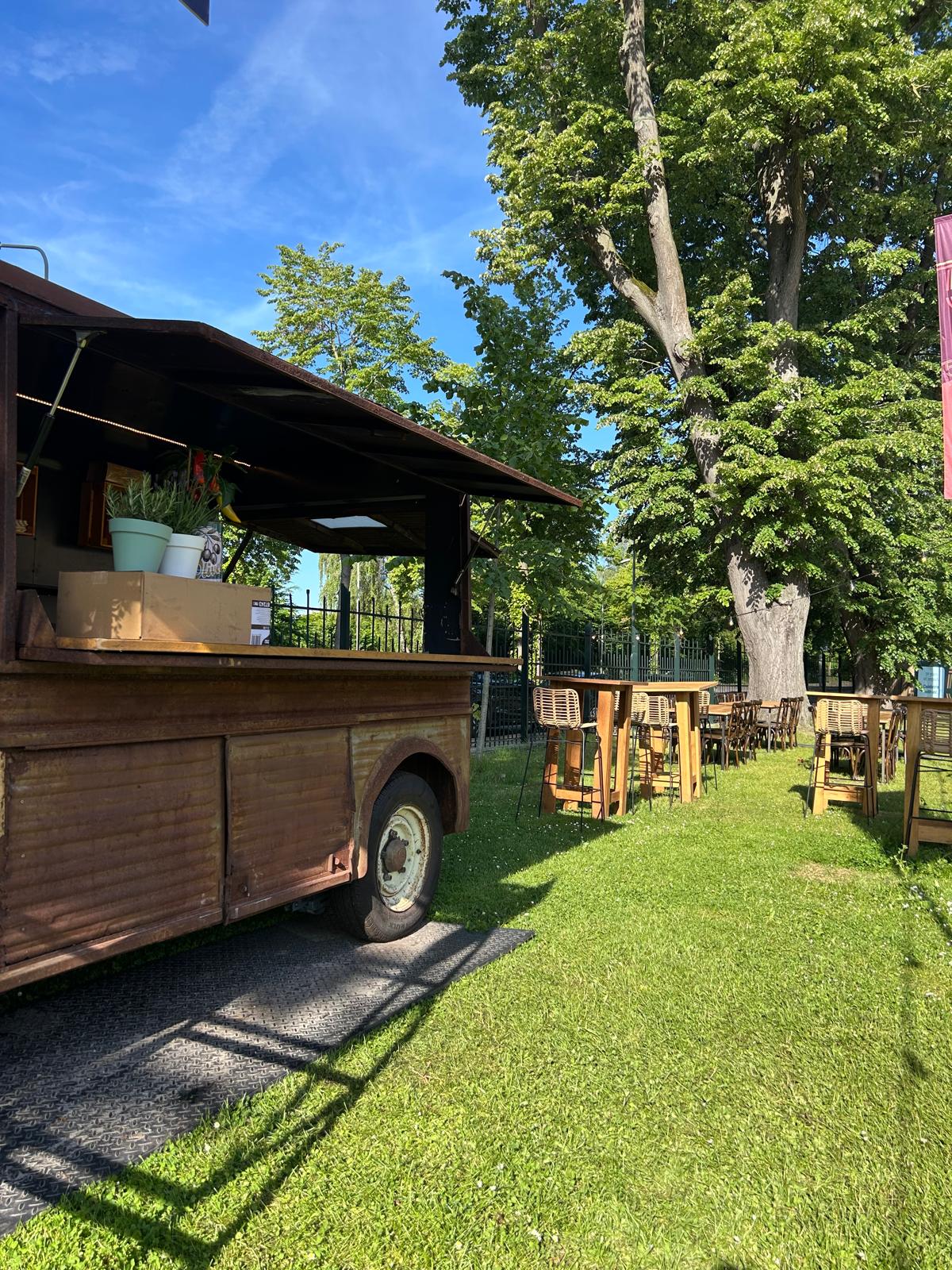 Houten foodtruck naast hoge tafels en barkrukken