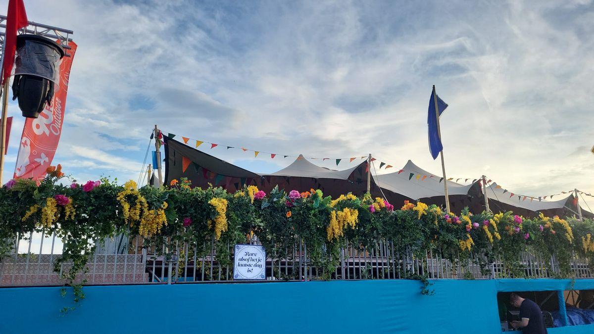 Festivaldecoratie met bloemenkransen langs een hek, stretchtent en vlaggetjes