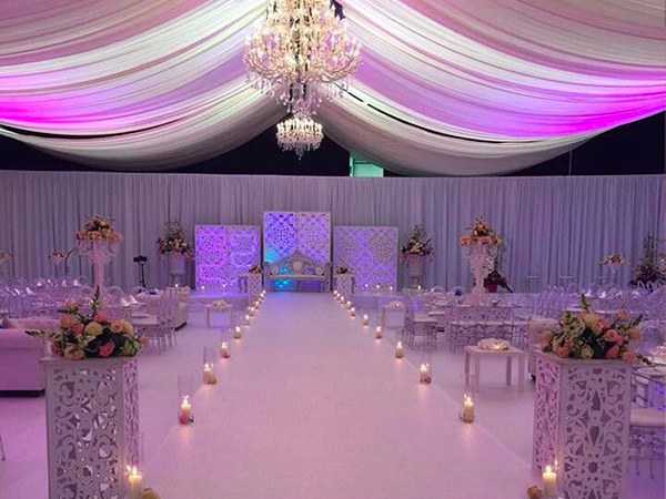 Wit bekleed podium met loopbrug, trappen, bloemen en kaarsen in een feesttent