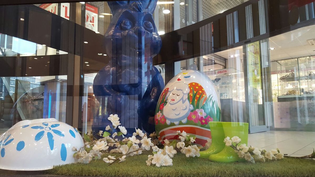 Paasdecoratie met grote paashaas, beschilderd paasei, bloesem en groene laarzen in een winkelcentrum