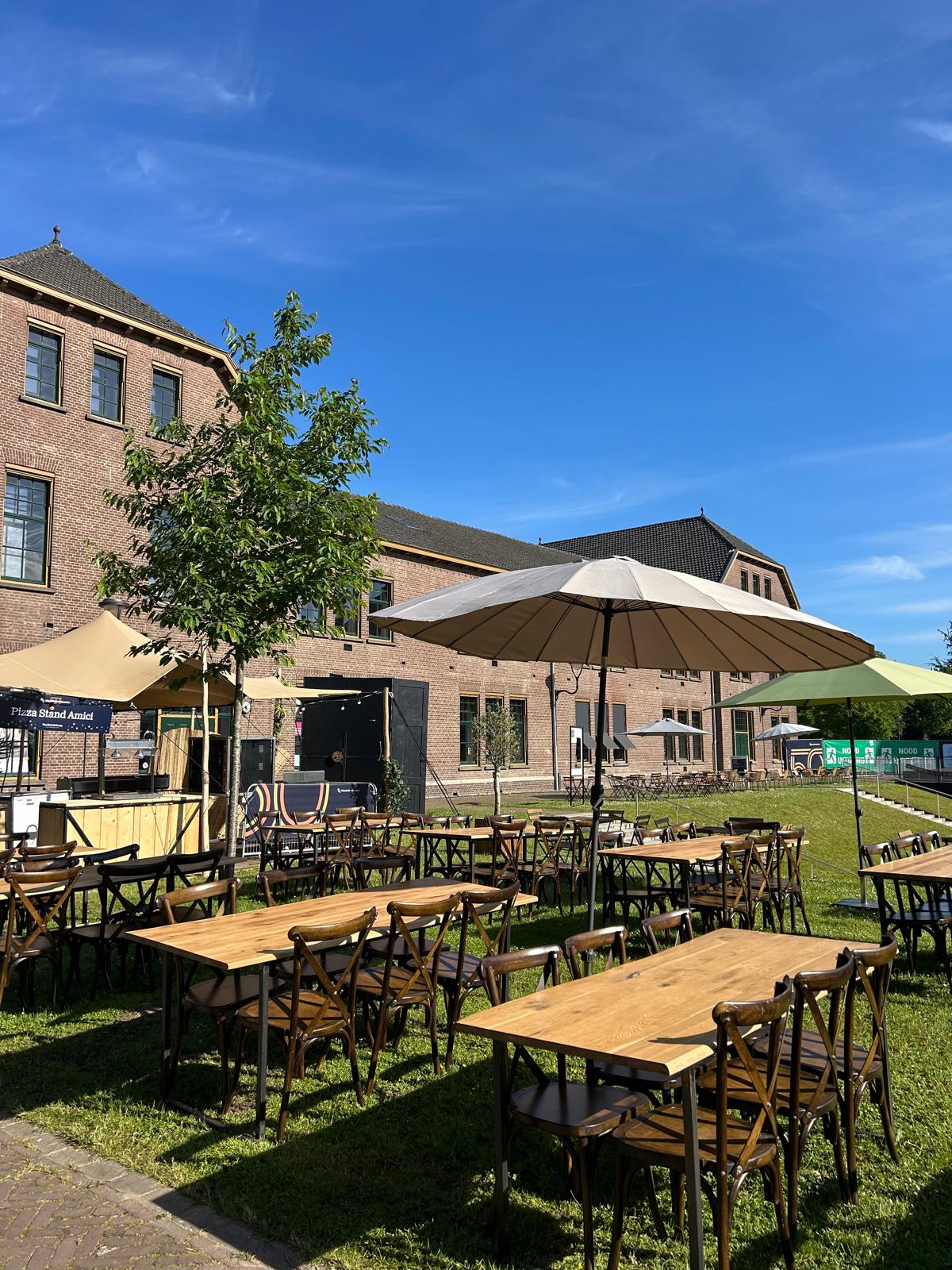 Lange houten tafels met kruisrugstoelen en grote parasols