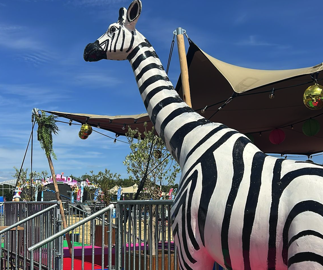 Zebra-strepen giraffe als eyecatcher op een kleurrijk festivalterrein