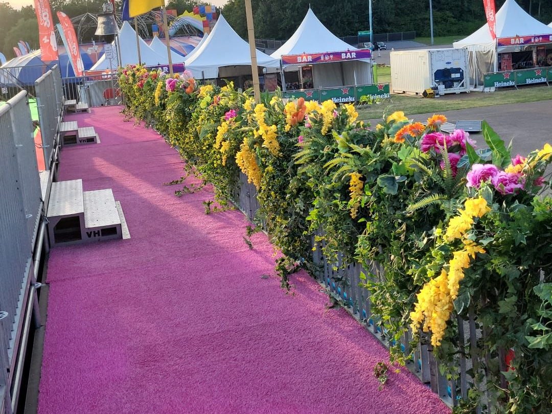Bloemenwand met gele en roze bloemen langs een roze loper op een festivalterrein