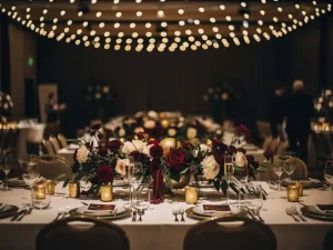Feestelijk versierde bedrijfsevenementenzaal met lange banquettafels, bloemstukken en gouden sfeerlichten aan het plafond.