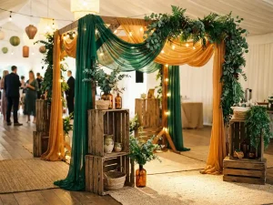 Feestelijk evenementstand met slingerverlichting, weelderig groen en houten kratten als decoratie in een warm verlichte zaal.