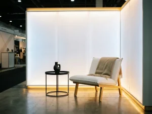 Minimalistische beursstand met witte lounge stoel, matte zwarte bijzettafel en warme sfeerverlichting op betonnen vloer.