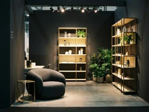 Minimalistische beurstand met sculptuurstoel, gouden decorobjecten en weelderig groen op gepolijste betonvloer.